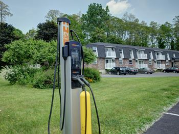 An electric vehicle charging station is located in a grassy area near apartment buildings.
